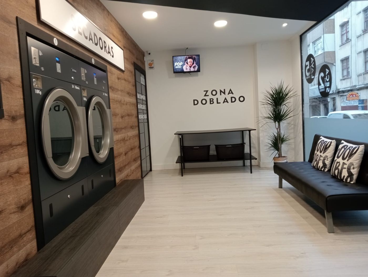 Vista general del local: sofá con libros y juegos a la izquierda, lavadoras y secadoras a la derecha